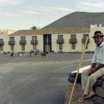 Pastor Majorero con su Ganado de Cabras Canarias y Lata en la Casa de los Coroneles - Foto de Francisco Rojas Fariña (Fachico) - Archivo de Fotografía Histórica de Canarias del Fondo para la Etnografía y el Desarrollo de la Artesanía Canaria (FEDAC) - Fedac.org - La Oliva - Fuerteventura - Archivo Documental de la Federación de Salto del Pastor Canario (FSPC) - Archipiélago Canario (Años 60 ó 70 del Siglo XX).